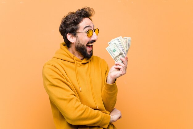 Joven cool con billetes de dólar contra la pared naranja