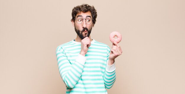 Joven cool con una rosquilla de azúcar rosa contra la pared plana