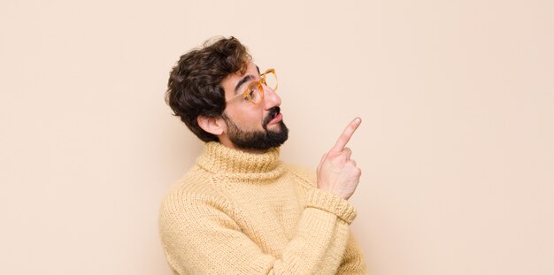 Joven cool sonriendo alegremente y mirando hacia los lados, preguntándose, pensando o teniendo una idea contra la pared plana