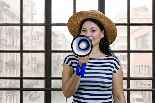 Joven coreana con sombrero de paja está dando un anuncio en las ventanas interiores a cuadros de megáfono atrás