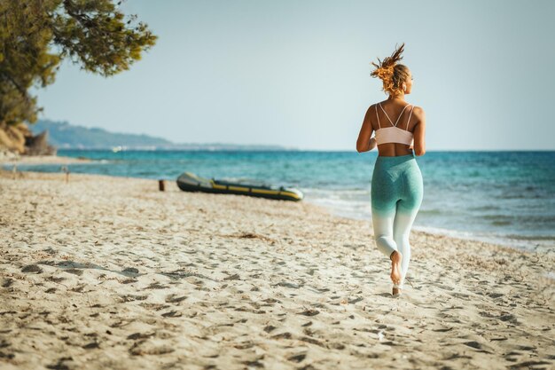 Una joven corre a lo largo de la orilla del mar en la playa durante el caluroso día de vacaciones de verano.