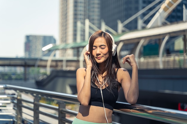 Joven corredor de mujer asiática descansando y escuchando música después de la sesión de entrenamiento en la mañana soleada.