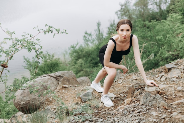 Joven corredora estirando brazos y piernas antes de correr en el sendero del bosque matutino cerca del lago