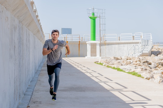 Joven corriendo por un paseo marítimo cerca de un faro del puerto