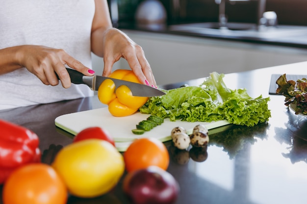 La joven corta verduras en la cocina con un cuchillo