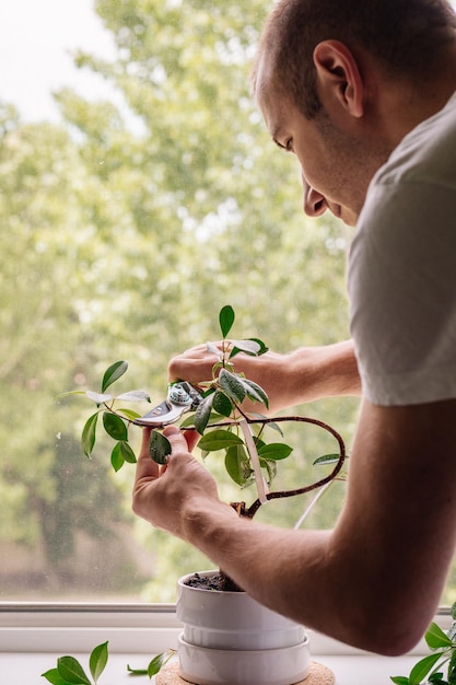 Un joven cortando una planta en maceta junto a la ventana de su casa