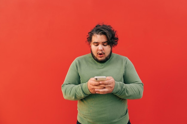 joven con un corte de pelo elegante está usando un teléfono inteligente para enviar mensajes de texto y chatear