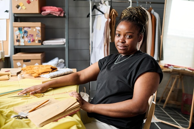 Joven costurera afroamericana o diseñadora de moda sentada junto a su lugar de trabajo