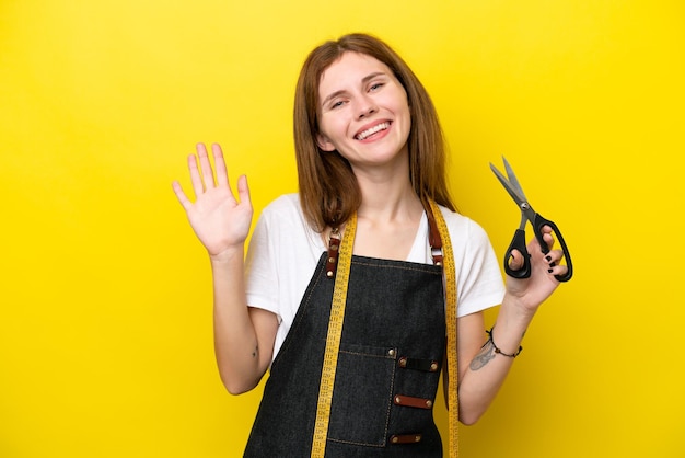 Joven costurera inglesa aislada de fondo amarillo saludando con la mano con expresión feliz