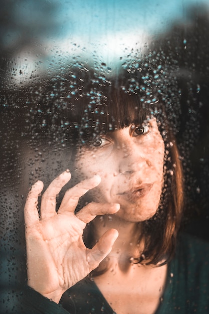 Una joven en cuarentena de la pandemia de Covid-19 en la ventana en un día lluvioso