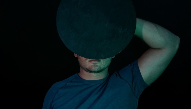 Un joven cubrió su cara con un disco redondo negro a la luz de neón en un estilo retro minimalismo negro