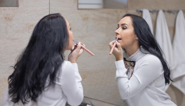 Una joven se cuida la cara a diario antes de ir a trabajar pinta sus labios con lápiz labial Morena en el baño preparándose para el trabajo