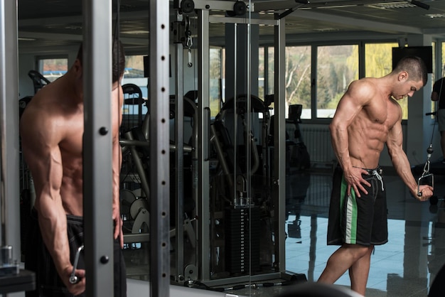 Joven culturista está trabajando en sus tríceps con cable en un gimnasio oscuro