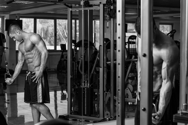 Joven culturista está trabajando en sus tríceps con cable en un gimnasio oscuro