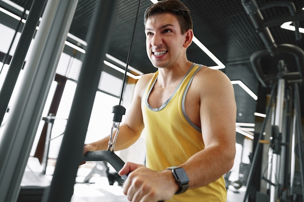 Joven culturista haciendo ejercicio de peso pesado para bíceps en un gimnasio