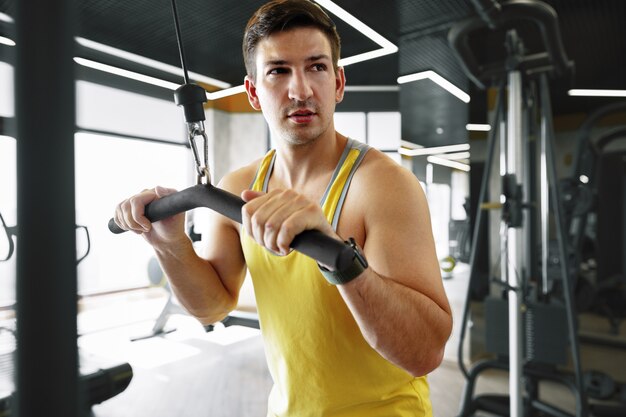 Joven culturista haciendo ejercicio de peso pesado para bíceps en un gimnasio