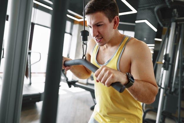 Joven culturista haciendo ejercicio de peso pesado para bíceps en un gimnasio