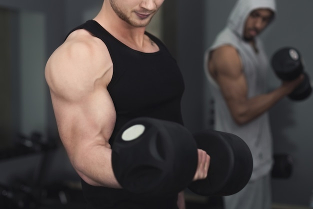 Joven culturista musculoso irreconocible haciendo peso muerto pesado en un moderno gimnasio. Hombre fuerte haciendo ejercicio con pesas en el gimnasio, espacio de copia, primer plano