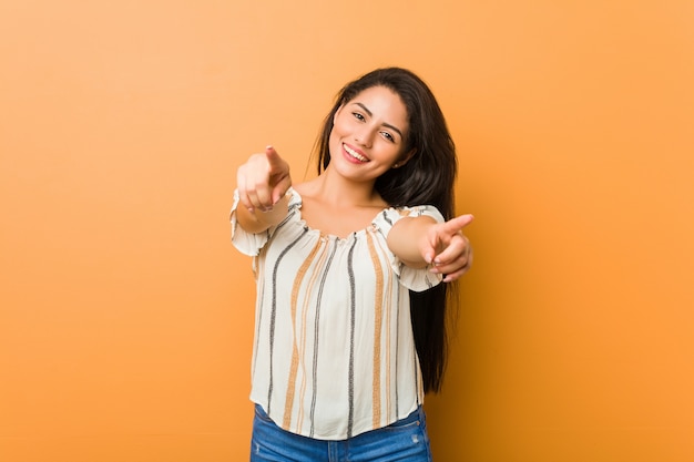 Joven con curvas sonrisas alegres apuntando al frente