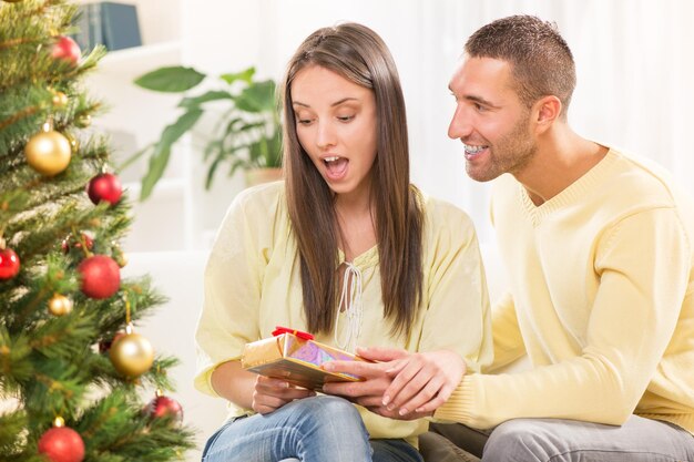 Joven dando un regalo sorpresa de Navidad a su bella novia.