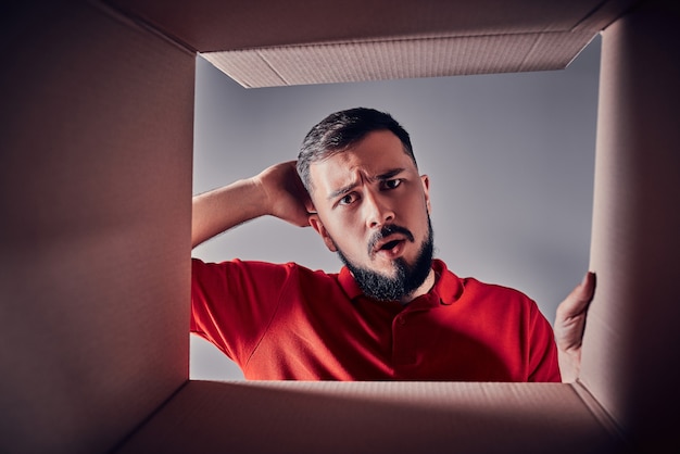 Foto joven decepcionado está buscando regalo dentro de una caja de cartón.