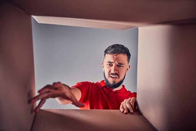 Joven decepcionado está buscando regalo dentro de una caja de cartón.