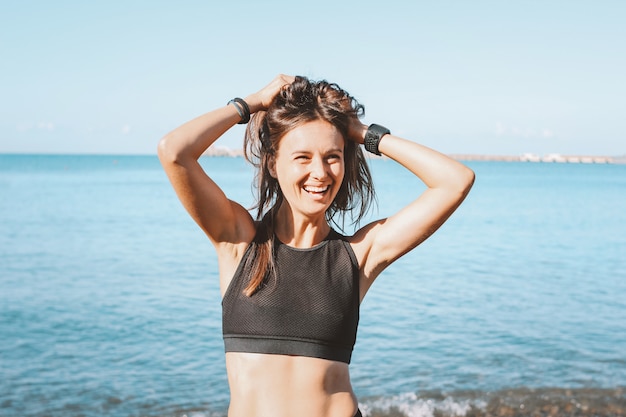 Joven delgada atlética cabello largo mujer feliz en ropa deportiva en la playa del mar en la mañana