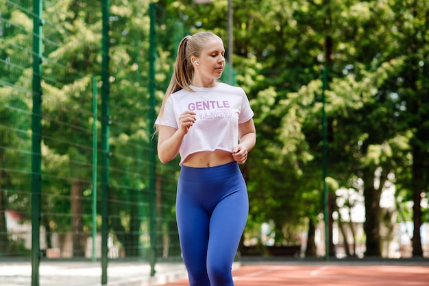Una joven delgada y deportiva con ropa deportiva corriendo al aire libre en el campo de deportes