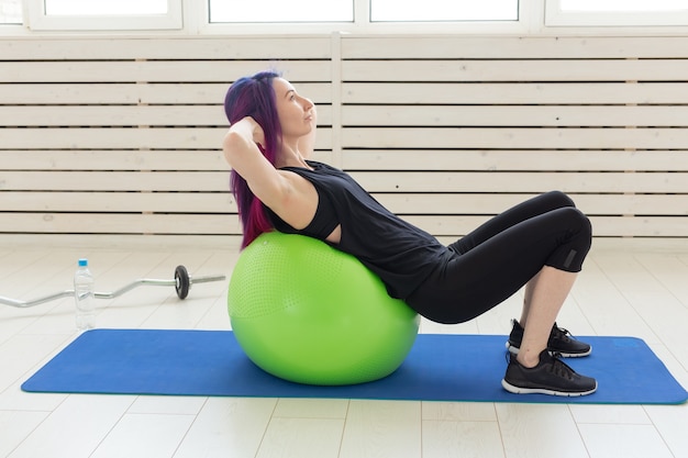 Joven delgada hace ejercicio y estiramiento de la espalda en un fitball verde en el gimnasio brillante