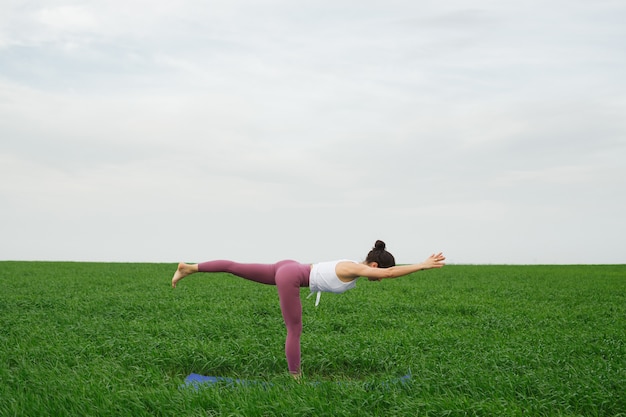 Joven delgada haciendo yoga al aire libre en un campo verde