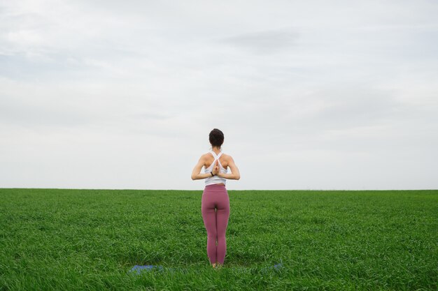 Joven delgada haciendo yoga al aire libre en un campo verde