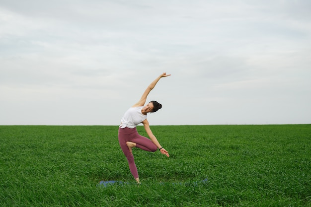 Joven delgada haciendo yoga al aire libre en un campo verde