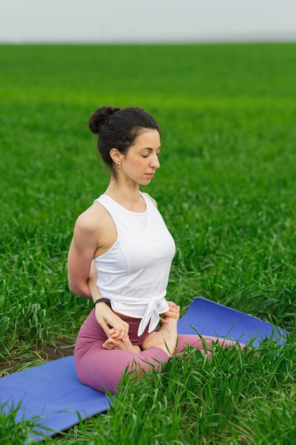 Joven delgada haciendo yoga al aire libre en un campo verde