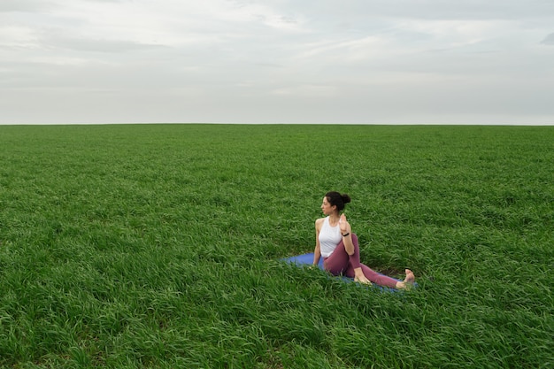 Joven delgada haciendo yoga al aire libre en un campo verde