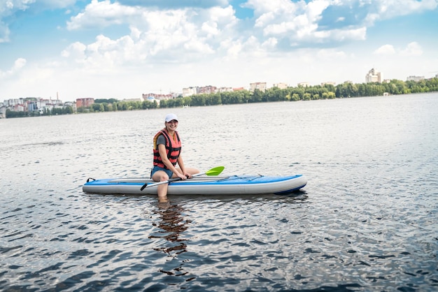 Una joven delgada monta una tabla de SUP en el lago de la ciudad y disfruta de un día caluroso de verano gratis