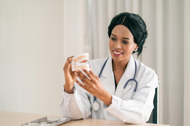 Joven dentista afroamericana o negra sosteniendo una dentadura postiza con cara feliz sonriendo