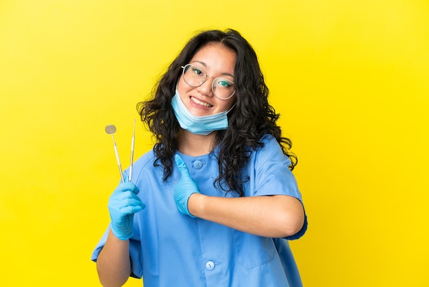 Joven dentista asiático sosteniendo herramientas sobre fondo aislado dando un pulgar hacia arriba gesto