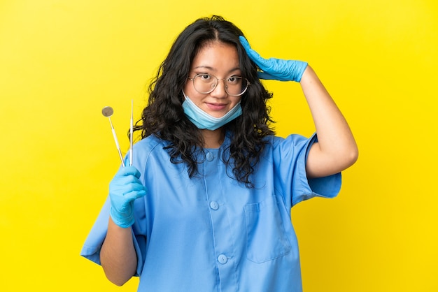 Joven dentista asiático sosteniendo herramientas sobre fondo aislado con expresión de sorpresa