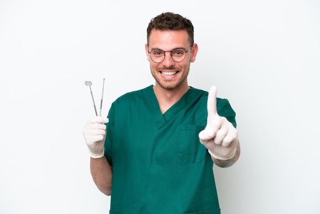 Joven dentista caucásico aislado de fondo blanco mostrando y levantando un dedo