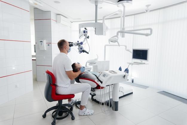 Un joven dentista examina y trata los dientes de un joven en la odontología blanca moderna usando un microscopio Tratamiento de prótesis dentales y blanqueamiento dental Prevención de caries