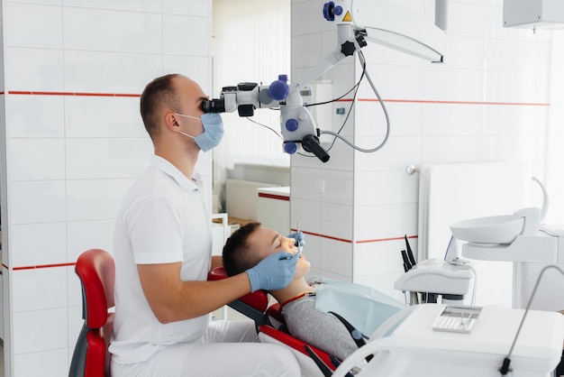 Un joven dentista examina y trata los dientes de un joven en la odontología blanca moderna usando un microscopio Tratamiento de prótesis dentales y blanqueamiento dental Prevención de caries