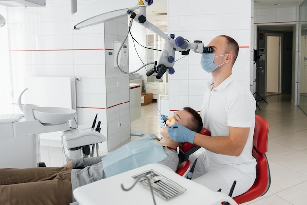 Un joven dentista examina y trata los dientes de un joven en la odontología blanca moderna usando un microscopio Tratamiento de prótesis dentales y blanqueamiento dental Prevención de caries