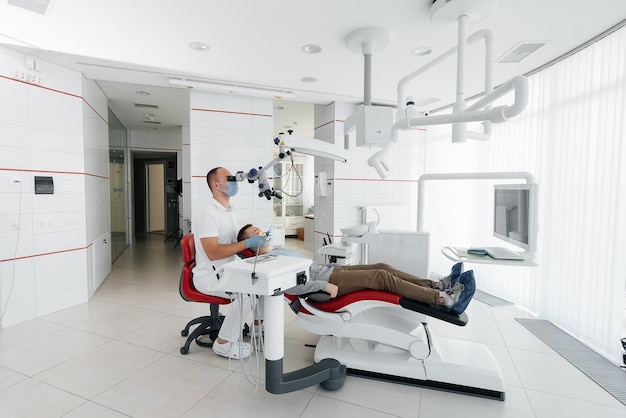 Un joven dentista examina y trata los dientes de un joven en la odontología blanca moderna usando un microscopio Tratamiento de prótesis dentales y blanqueamiento dental Prevención de caries