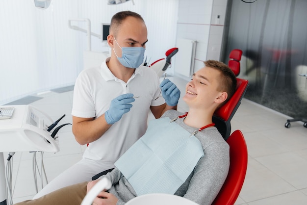 Un joven dentista examina y trata los dientes de un joven en un primer plano de odontología blanca moderna Tratamiento de prótesis dentales y blanqueamiento dental Odontología moderna Prevención
