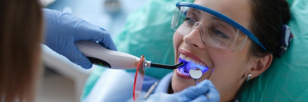 Joven dentista en guantes protectores revisando la lámpara de fotopolímero de fijación del sello dental durante el estoma