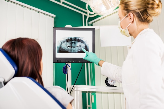 Joven dentista mostrando al paciente una imagen de rayos X en la pantalla LCD.