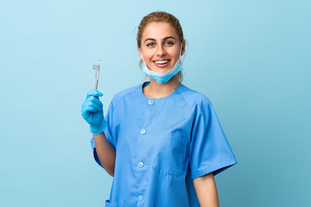 Joven dentista sosteniendo herramientas sobre aplausos azules aislados