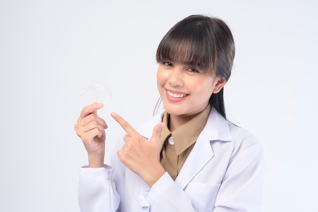 Una joven dentista sosteniendo llaves invisalign sobre un estudio de fondo blanco, salud dental y concepto de ortodoncia.