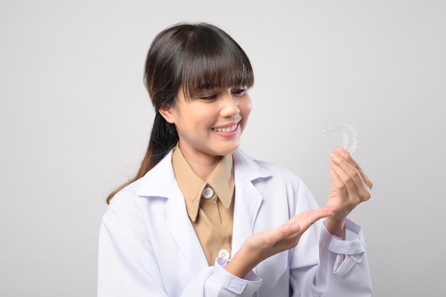 Una joven dentista sosteniendo llaves invisalign sobre un estudio de fondo blanco, salud dental y concepto de ortodoncia.