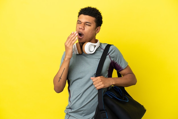 Joven deporte afroamericano con bolsa de deporte aislado sobre fondo amarillo bostezando y cubriendo la boca abierta con la mano